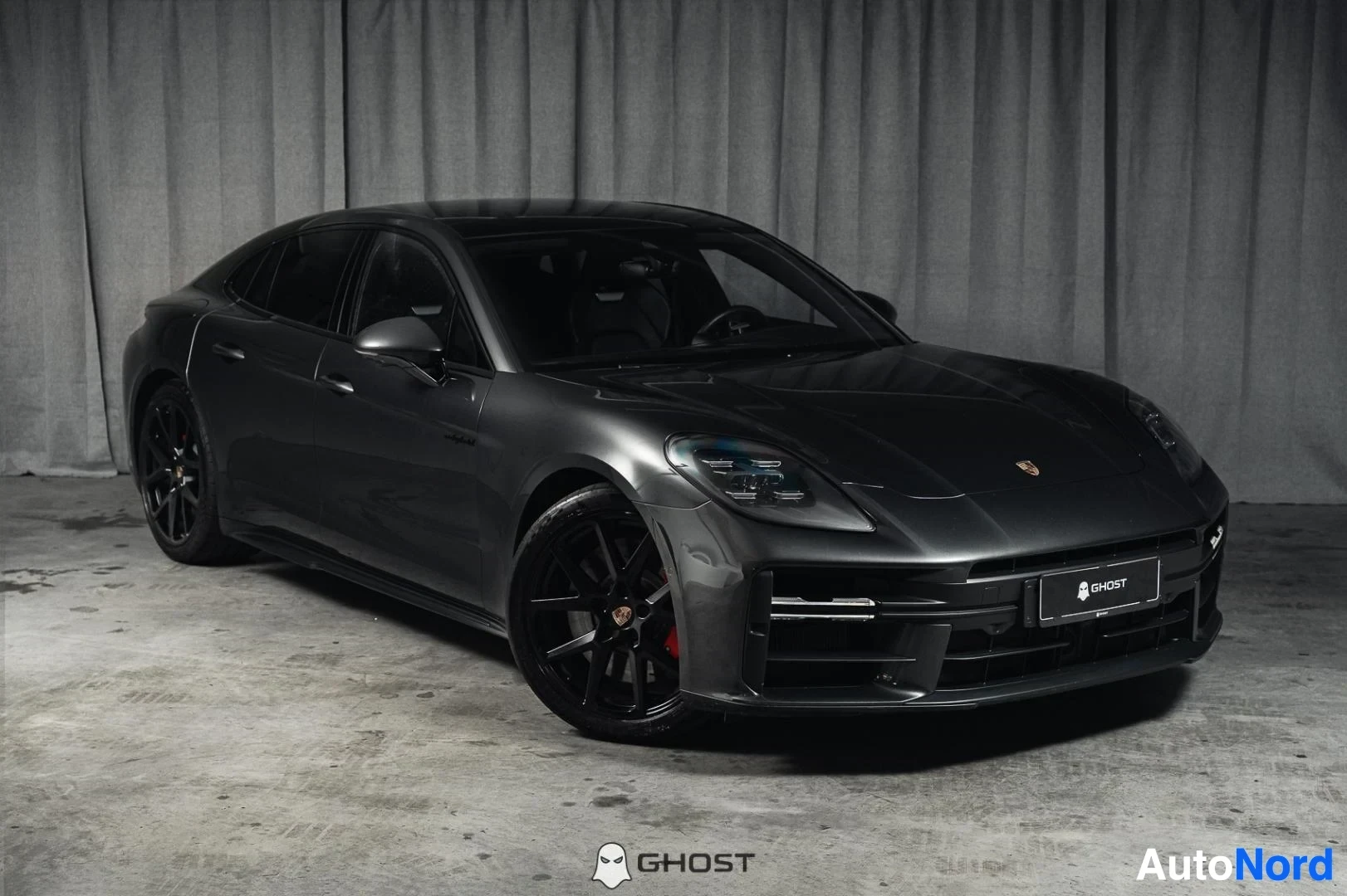 Etuviisto, nokka oikealle: Tummanharmaa Porsche Panamera, koko ajoneuvo näkyvissä, mustat vanteet, studiotausta