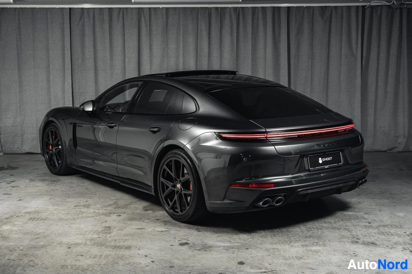 Takaviisto: Tummanharmaa Porsche Panamera, koko ajoneuvo näkyvissä, mustat vanteet, studiotausta