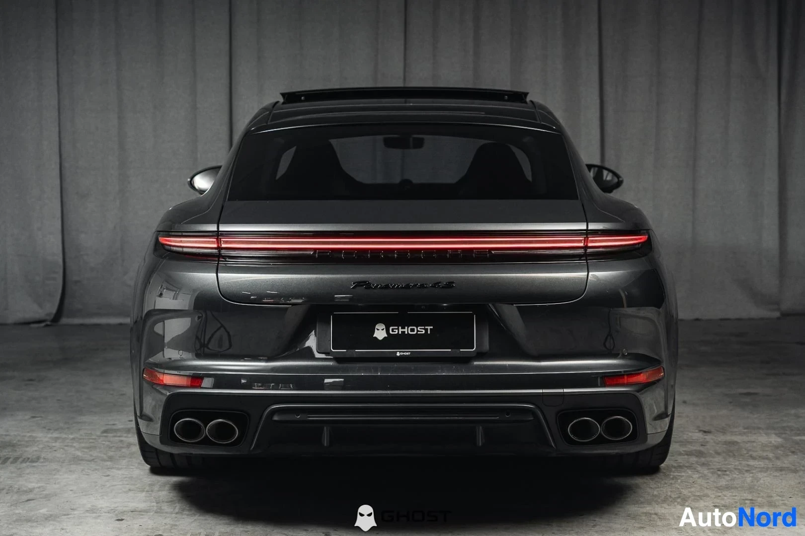 Takaa: Tummanharmaa Porsche Panamera, koko ajoneuvo näkyvissä, takavalopalkki ja neljä pakoputken päätä, studiotausta