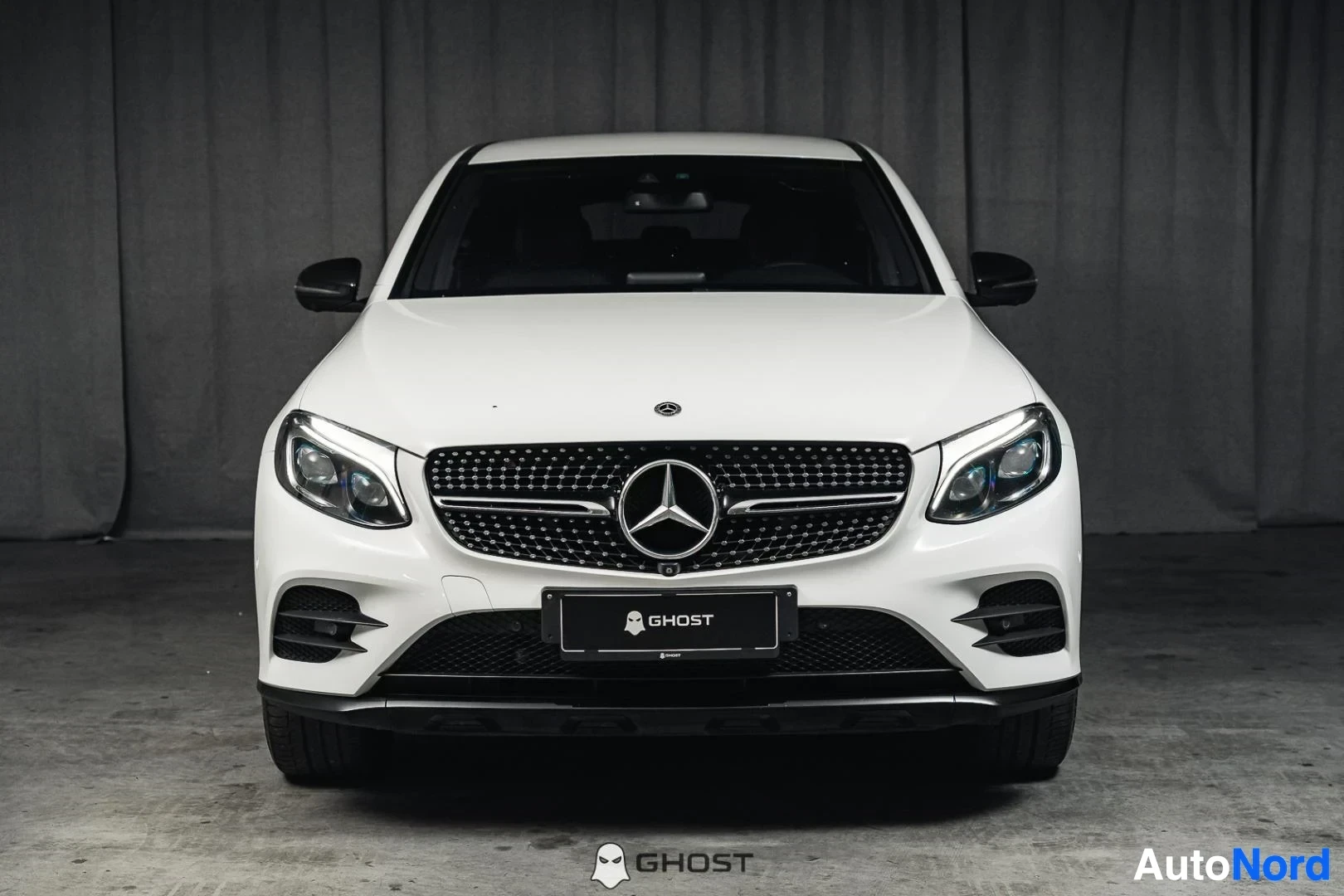 Edestä: Valkoinen Mercedes-Benz GLC 350e coupé, koko ajoneuvo näkyvissä, ajovalot päällä, studiotausta