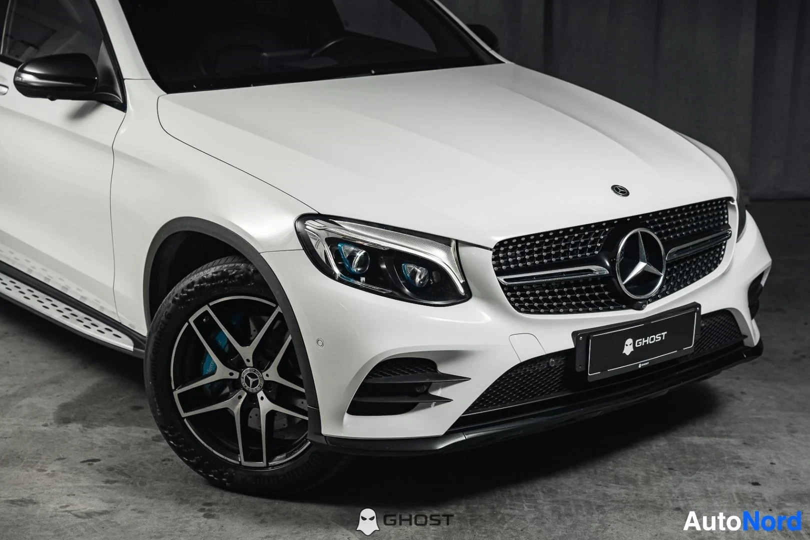 Etuviisto, nokka oikealle: Valkoinen Mercedes-Benz GLC 350e coupé, lähikuva keulasta ja tummasta etuvanteesta