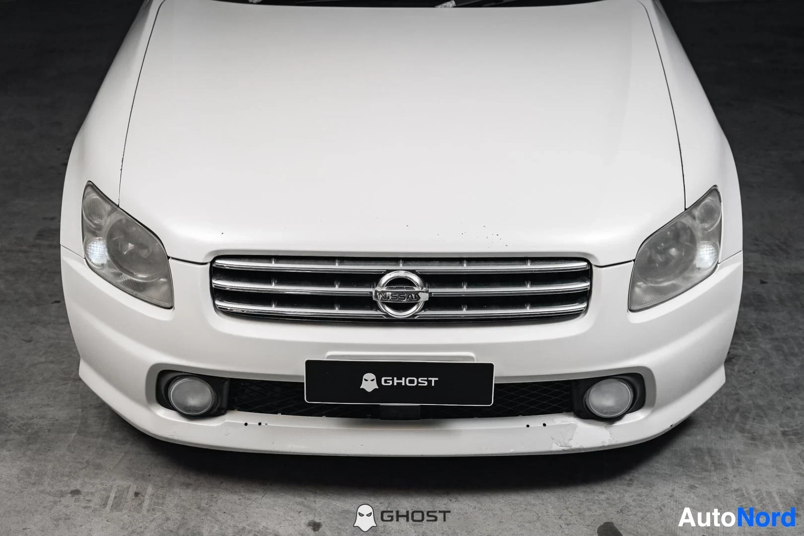 Edestä: Valkoinen Nissan Stagea, lähikuva keulasta, säleikkö ja sumuvalot