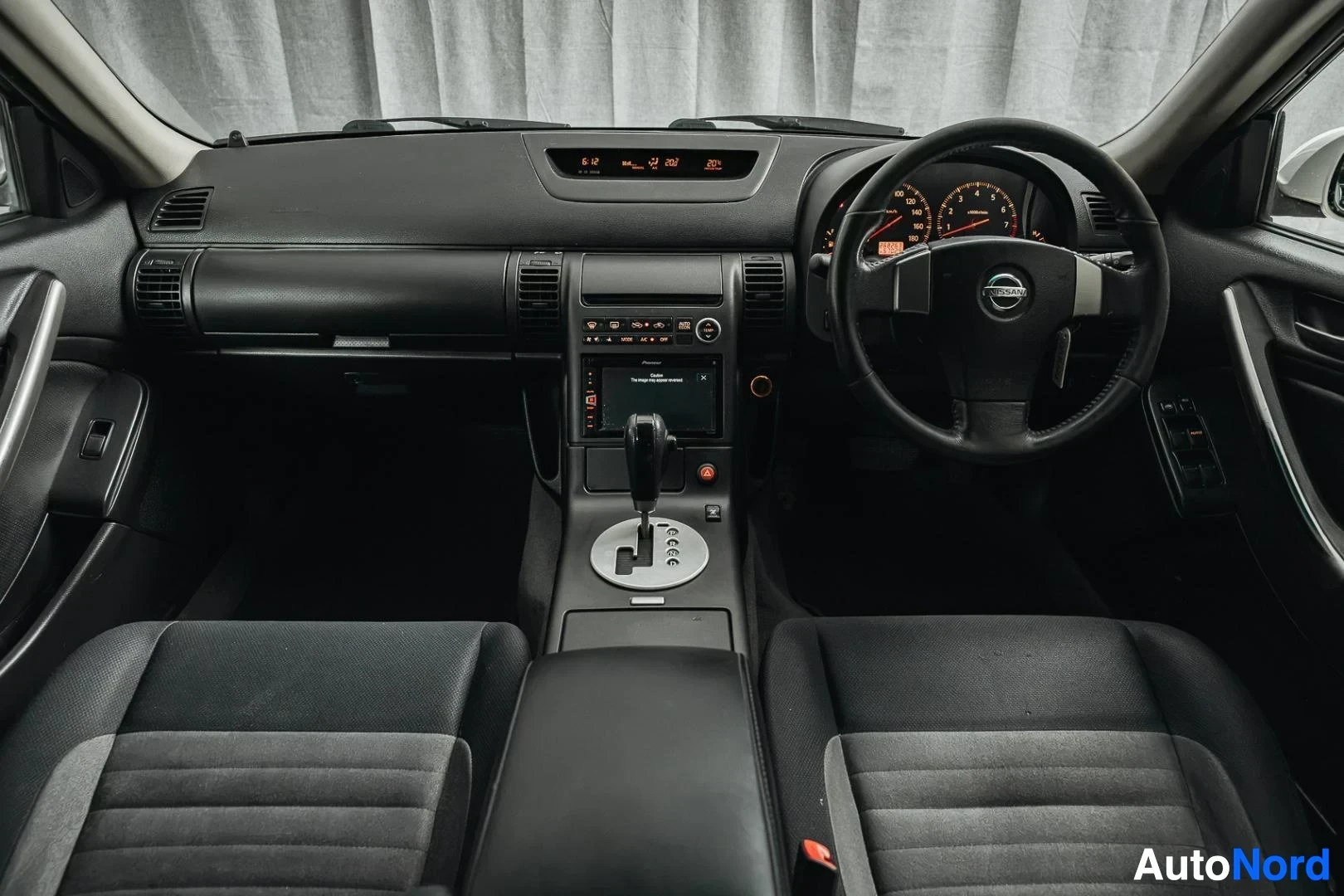 Ohjaamo: Valkoinen Nissan Stagea, kojelauta, ohjauspyörä ja keskikonsoli, automaattivaihteisto