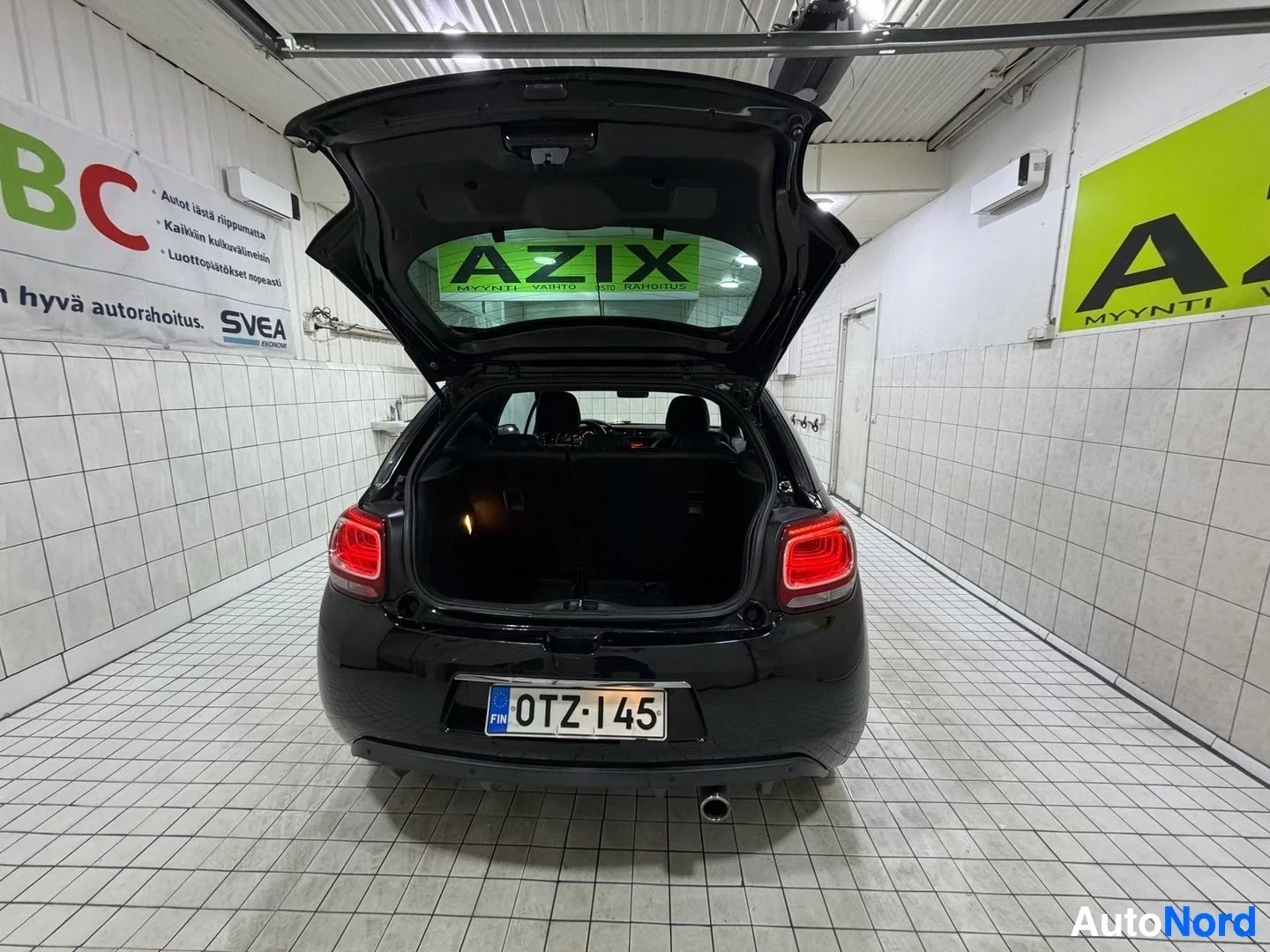 Takaa: Musta Citroën DS3 takaapäin kuvatussa, rekisterinumero, takaluukku auki, punaiset takavalaisimet näkyvissä, pysäköity halliin