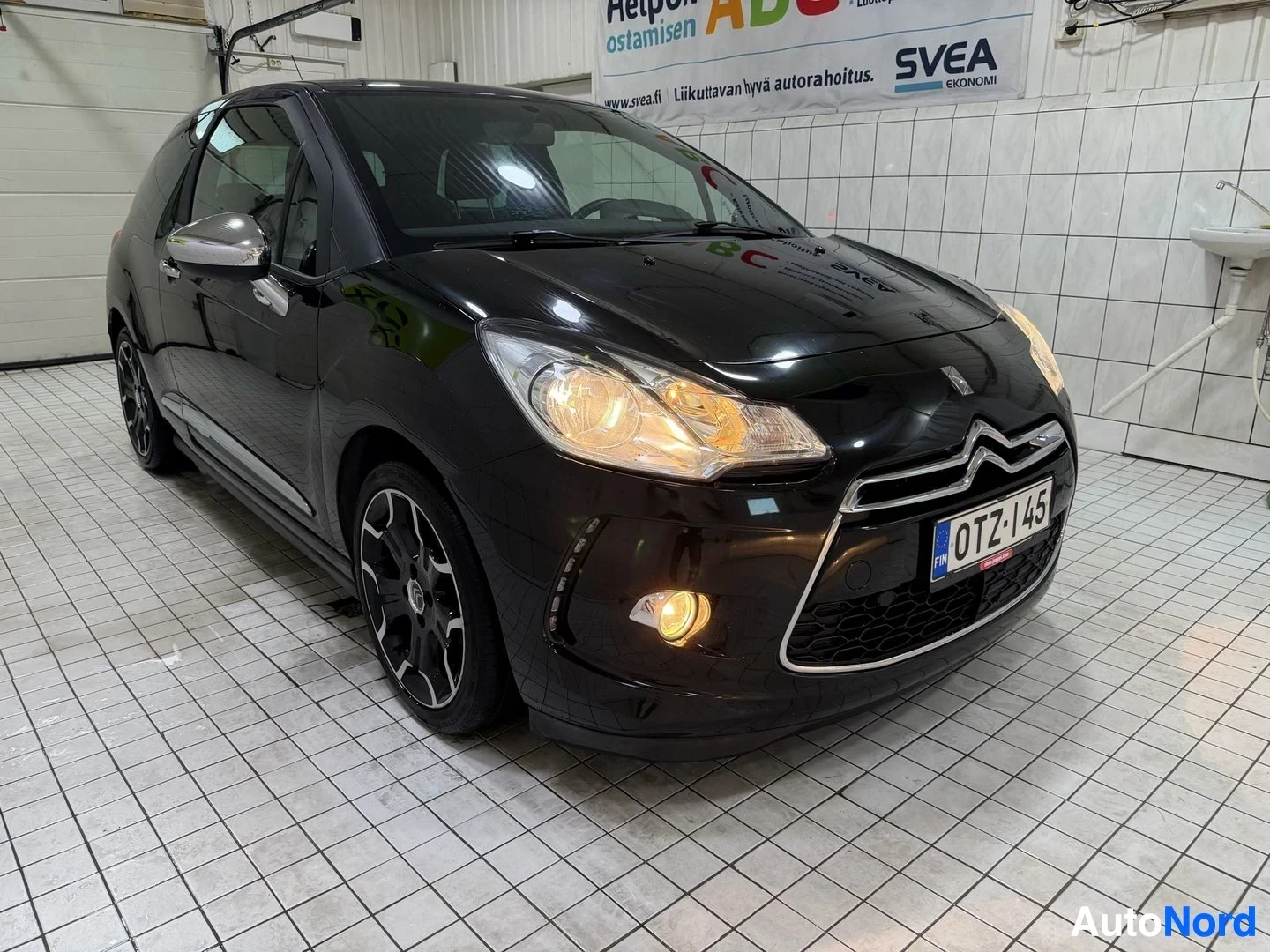Etuviisto, nokka vasemmalle: Musta Citroën DS3 pysäköitynä halliin, etunäkymä hieman vasemmalta. Rekisterikilpi näkyy. Autolla on LED-päivävalot, valkoiset vanteet ja siipi