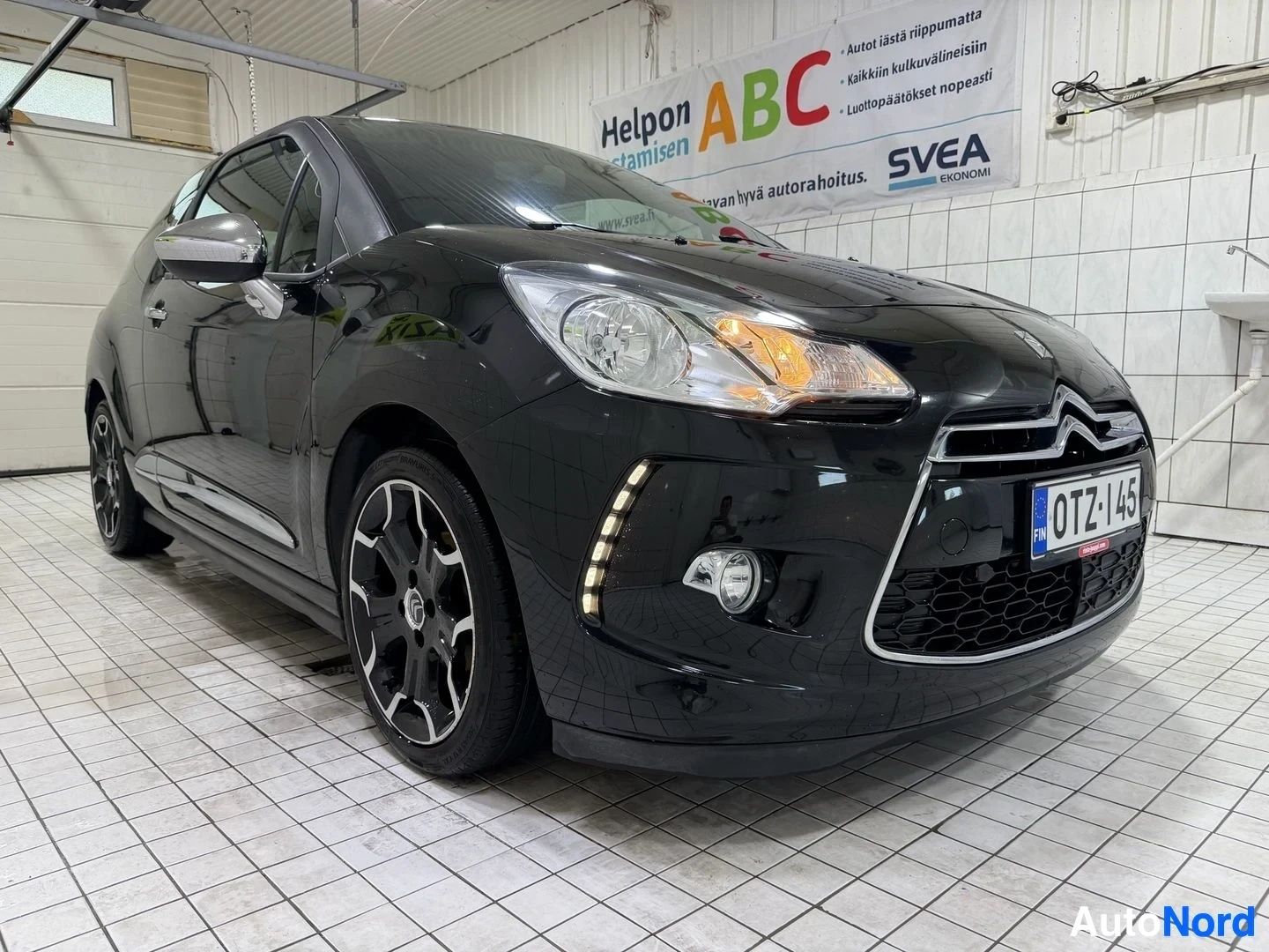 Etuviisto, nokka oikealle: Musta Citroën DS3 pysäköitynä halliin, etunäkymä hieman oikealta. Rekisterikilpi näkyy. Autolla on LED-päivävalot, valkoiset vanteet ja siipi ava