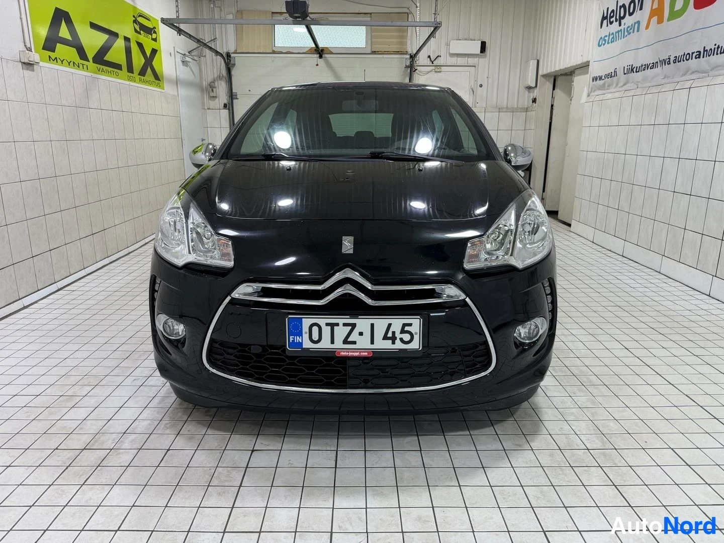 Edestä: Musta Citroën DS3 etukuva suoraan autotallissa, rekisterikyltti keskellä, etupuskuri, säleikköverkko ja pyöreät etuvaloyksiköt näkyvät selvästi