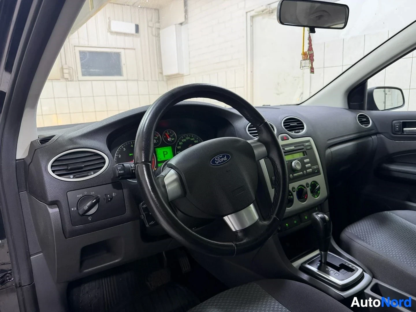 Ohjaamo: Auton sisäpuoli sivusta, näkyy ohjauspyörä Ford-logolla, instrumentit vihreällä näytöllä ja keskikonsoli
