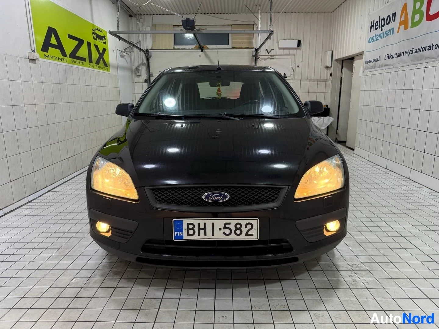 Edestä: Musta Ford Focus suoraan edestä, autolla on LED-päiväajot päällä ja alumiinivanteilla, pysäköity huoltohallin sisälle