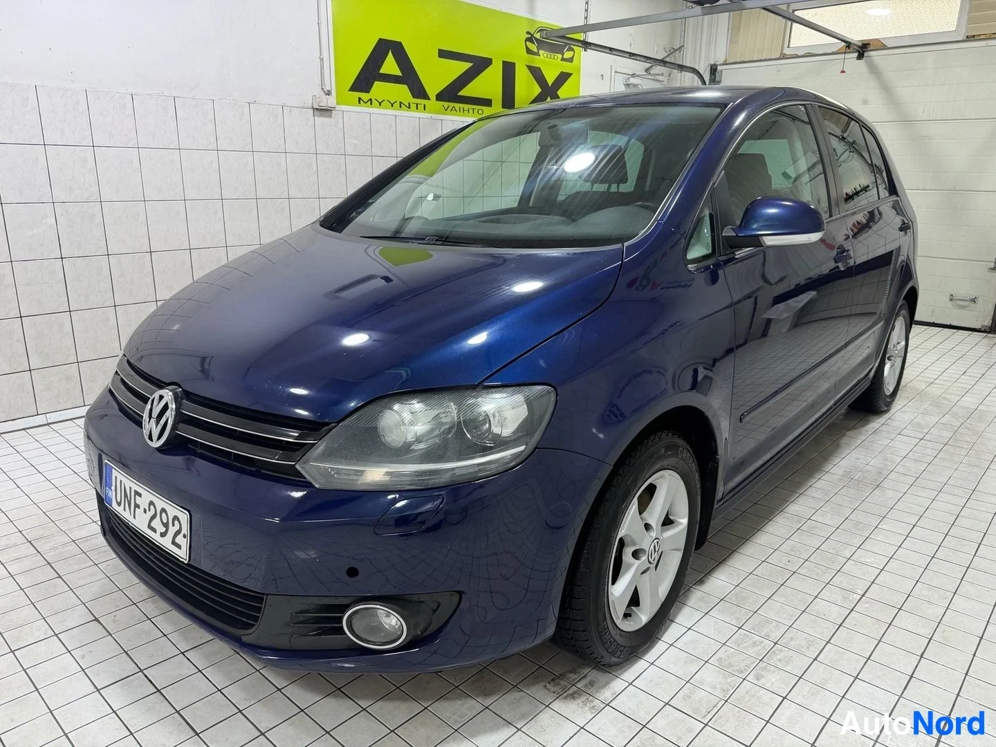 Etuviisto, nokka oikealle: Tummansininen Volkswagen Golf Plus etuvasemmalta kuvattuna. Auton etuosassa näkyy rekisterikilpi "". Etupuskurissa on pyöreät sumuvalot. Autossa o