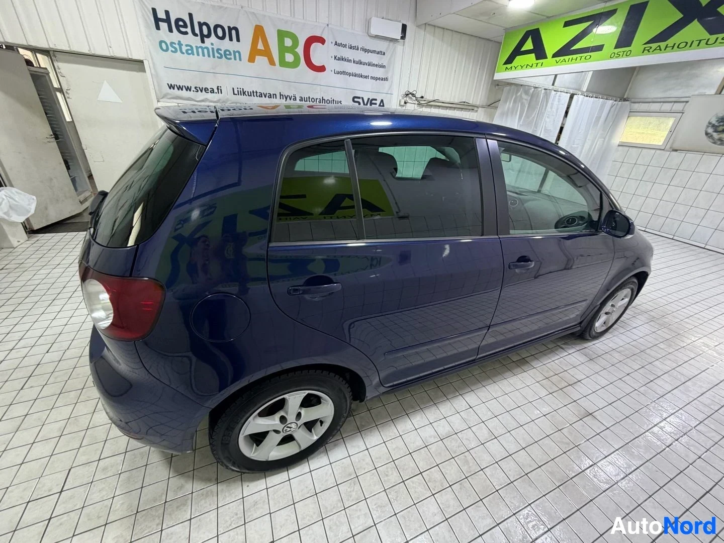 Takaviisto: Tummansininen Volkswagen Golf Plus takaviistosta oikealta puolelta kuvattuna. Auton takaosassa näkyy takavalot ja takalasinpyyhin. Oikea takaovi on näkyvissä. A