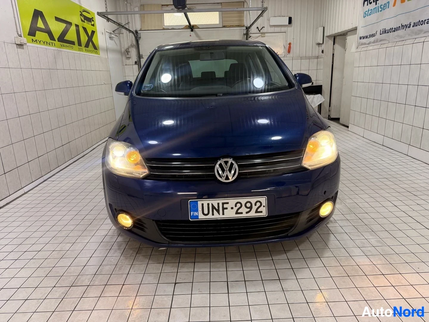 Edestä: Edestä kuvattu sininen henkilöauto valkoisessa hallissa. Auton rekisterinumero on ja siinä näkyy Volkswagen-logo