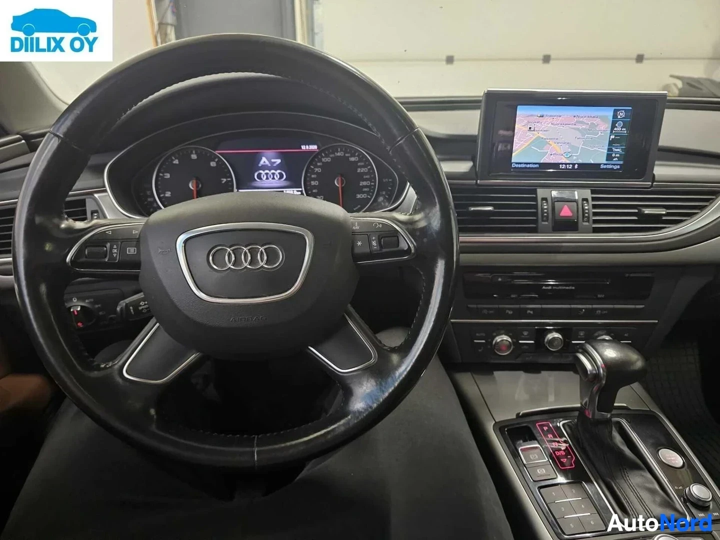 Ohjaamo: Auton sisätila: Audi-painikkeella varustettu ohjauspyörä, värinäyttö-mittaristo sekä navigointilaite näkyvissä.