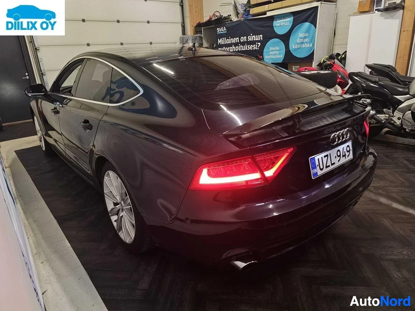 Takaviisto: Tummanpunainen Audi viistoperä sisätiloissa, kylkiprofiilissa ja taakaa näkyvillä LED-takavaloilla, rekisterikilpi
