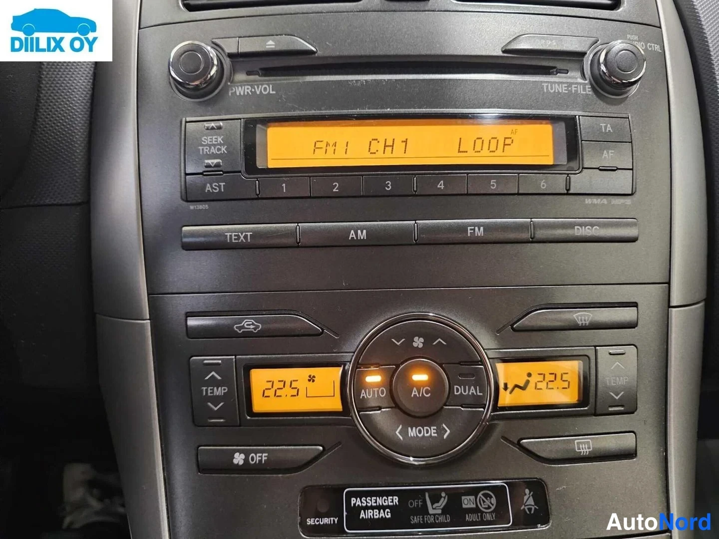 Muu: Kojelaudan radion ja ilmastoinnin paneeli lähikuvassa: radion näytöllä 'FM1 CH1 LOOP', painikkeet TEXT, AM, FM, DISC, sekä A/C- ja DUAL-ilmastointipainikkeet, j