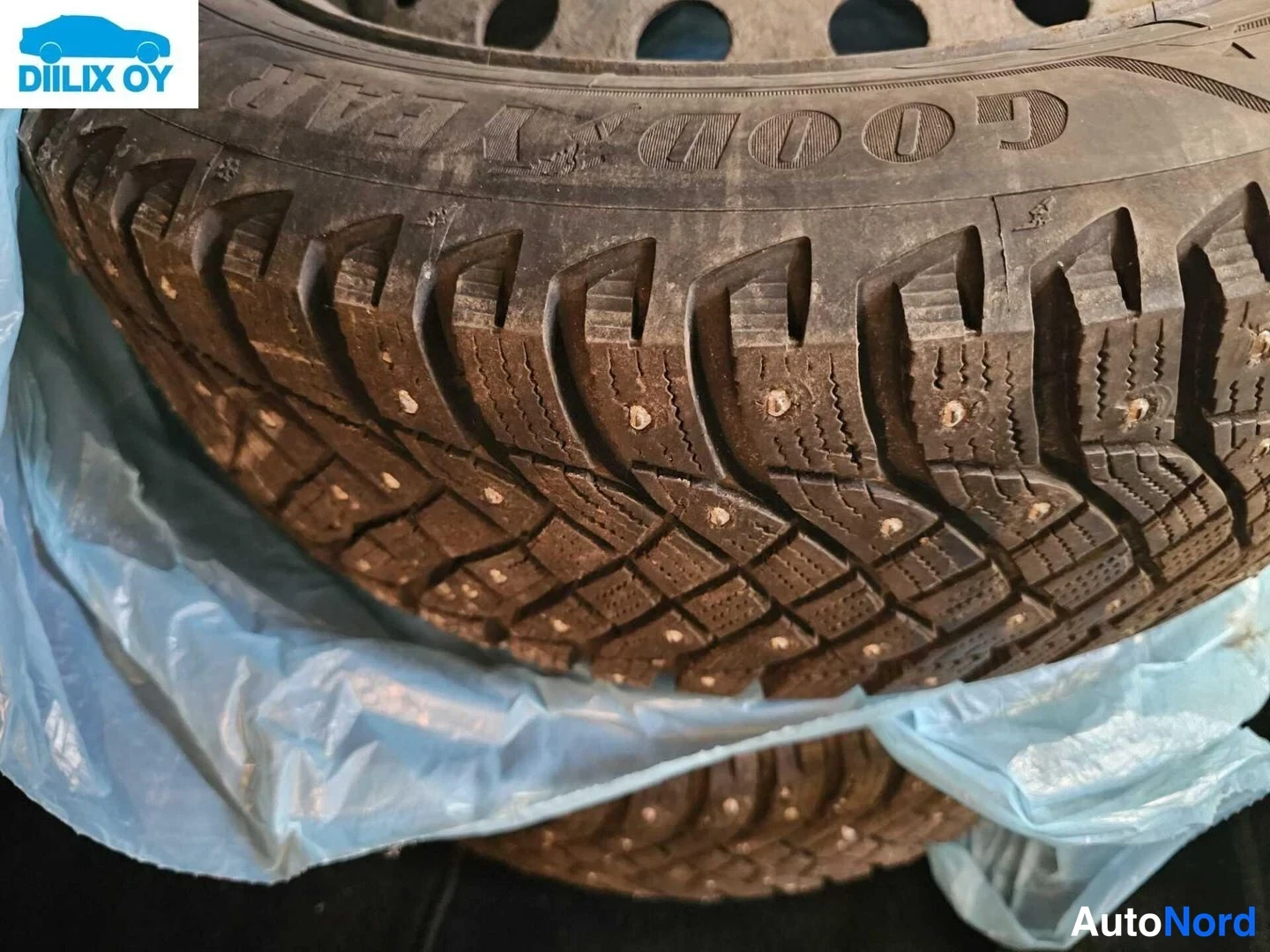 Muu: Nastarenkaiden lähikuva, päällimmäisen renkaan sivuseinässä lukee 'GOODYEAR'; renkaat on piilotettu sinisen muovipussin alle.