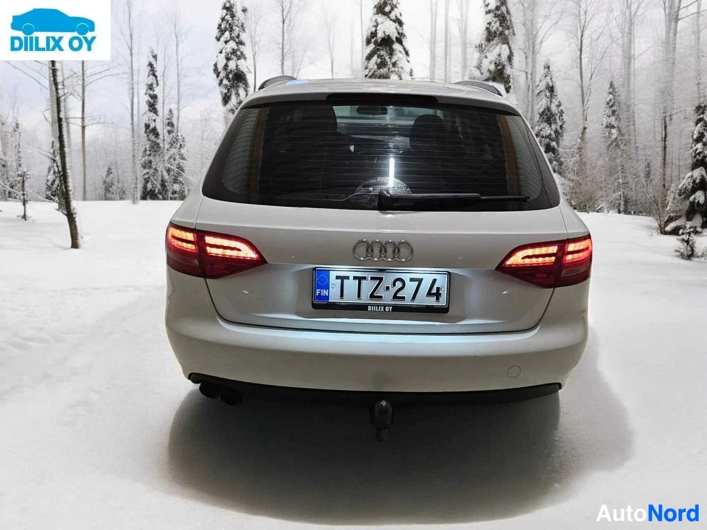 Takaa: Valkoinen Audi-farmari takaosasta kuvattuna, rekisterikilvessä, takaosassa vetolaitteella, lumisella metsäalueella