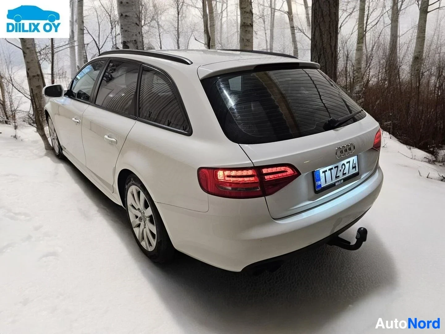 Takaviisto: Valkoinen Audi-farmari sivusta, rekisterikilvessä, takaosassa vetolaitteella, lumisella metsäalueella