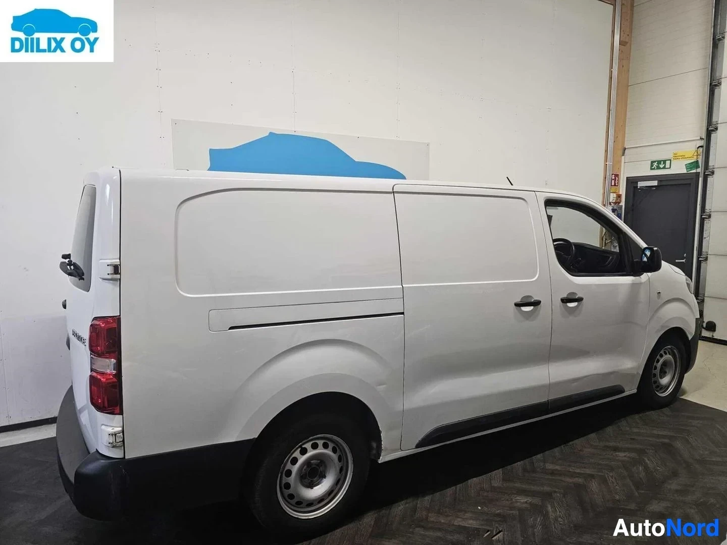 Sivulta: Valkoinen Toyota Proace -pakettiauto varastotiloissa profiilista vasemmalta, näkyy koko sivu ja taka