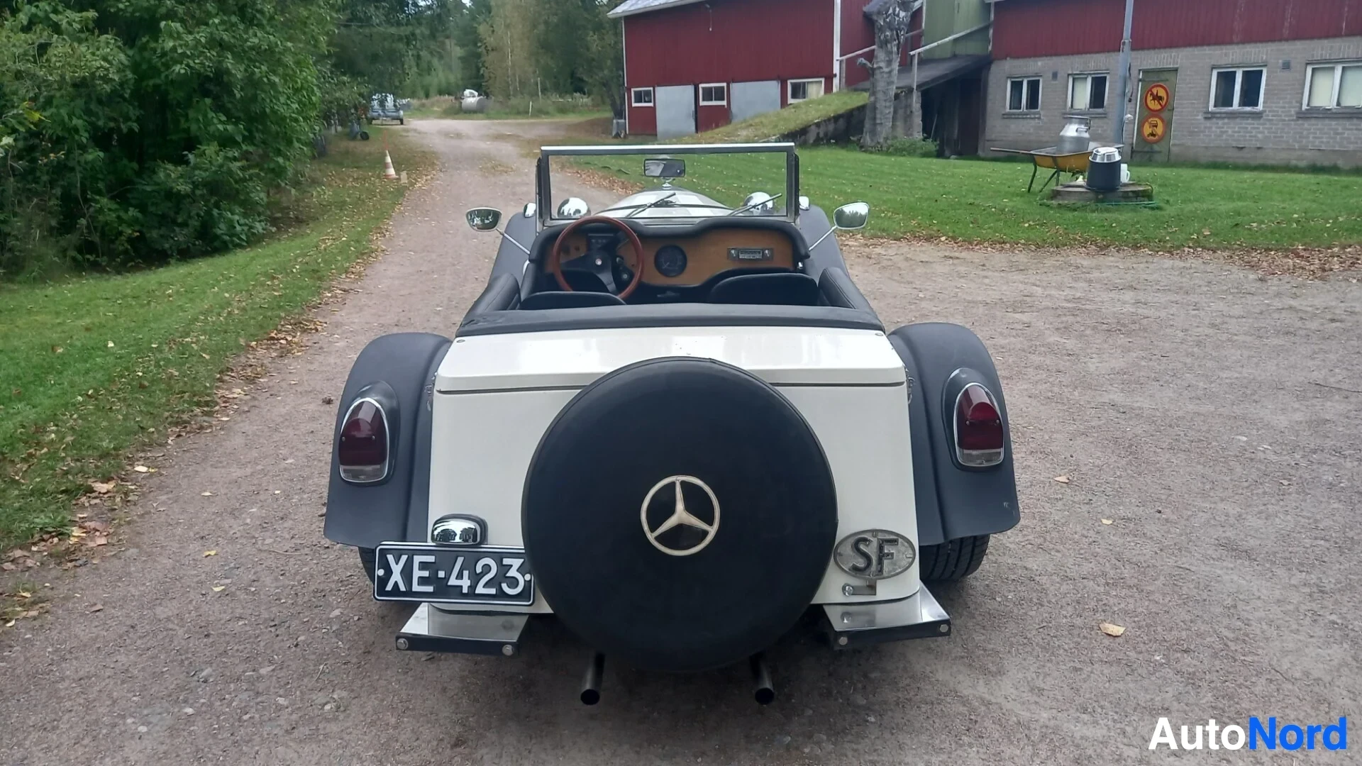 Takaa: Valkoinen avoauto mustilla lokasuojilla ja vararenkaalla perässä. Auton rekisterikilpi on XE-423. Taustalla rakennuksia ja puita.