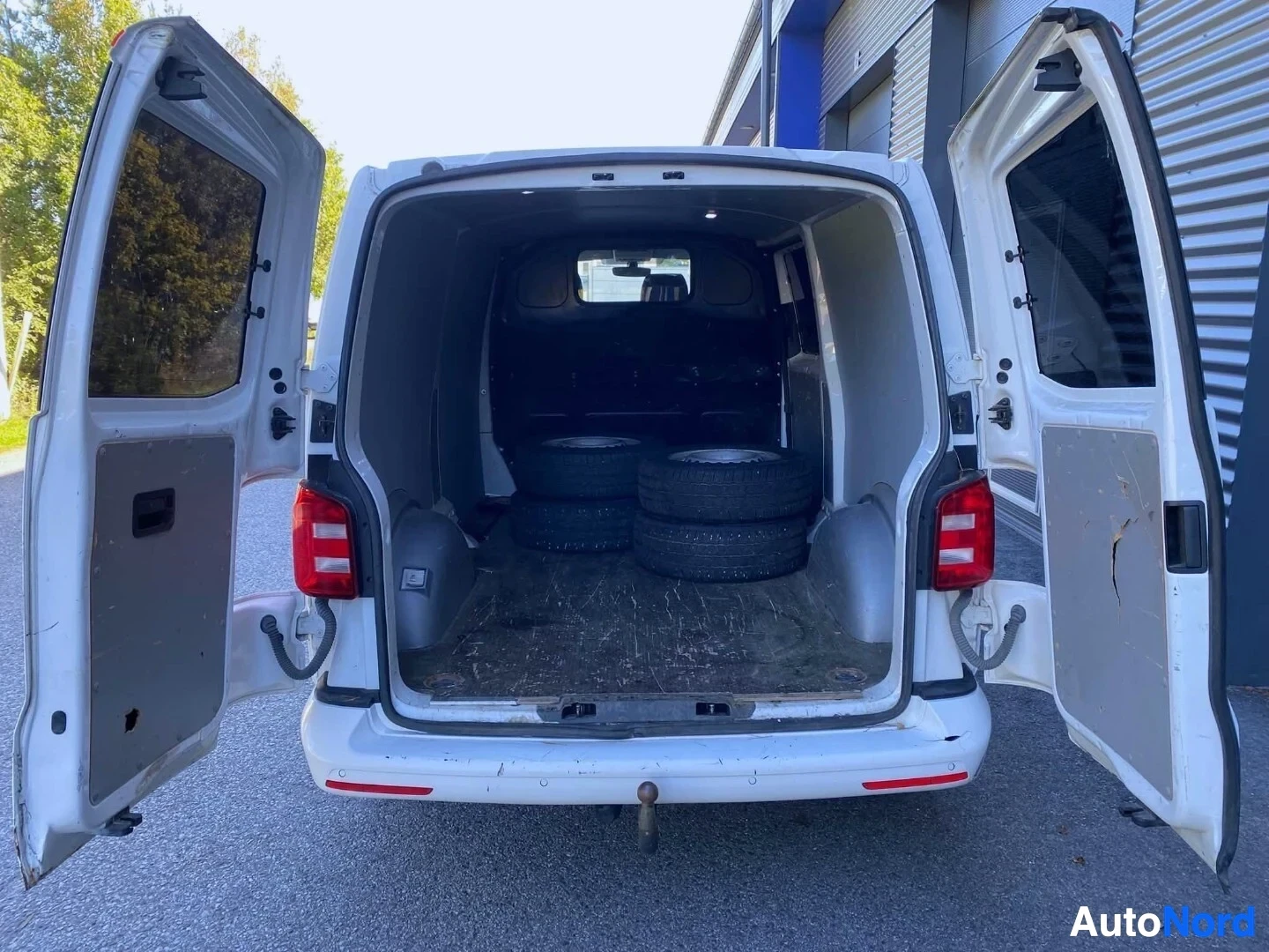 Takaa: Takaa kuvattu valkoinen pakettiauto, jossa takaovet ovat auki ja tavaratilassa on neljä rengasta pinottuna.