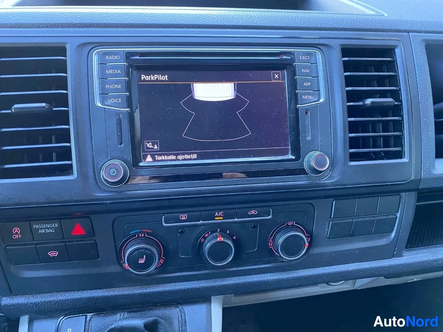 Ohjaamo: Kuva auton infotainment-järjestelmän näytöstä, jossa näkyy pysäköintitutkan ParkPilot-näkymä ja varoitusteksti. Ilmastoinnin säätimet ovat näkyvissä näytön alap