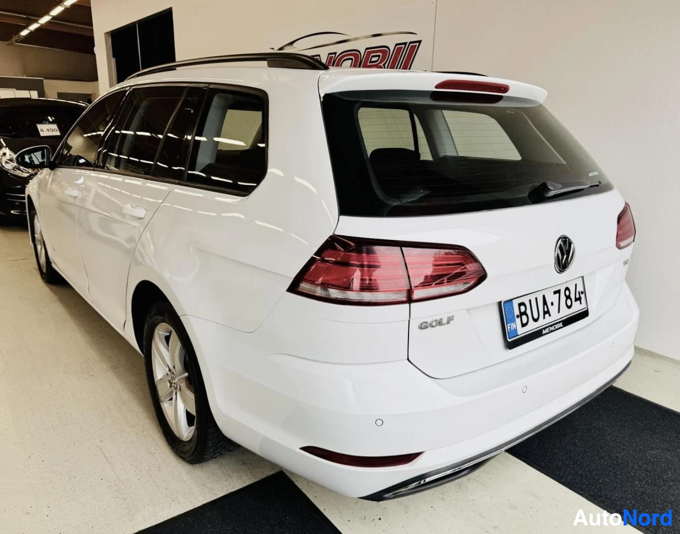Takaviisto: Valkoinen Volkswagen Golf Variant kuvattuna takaa ja oikealta puolelta, perä osoittaa kuvan vasempaan reunaan. Autossa on kattokaiteet ja takana parkkitutka.