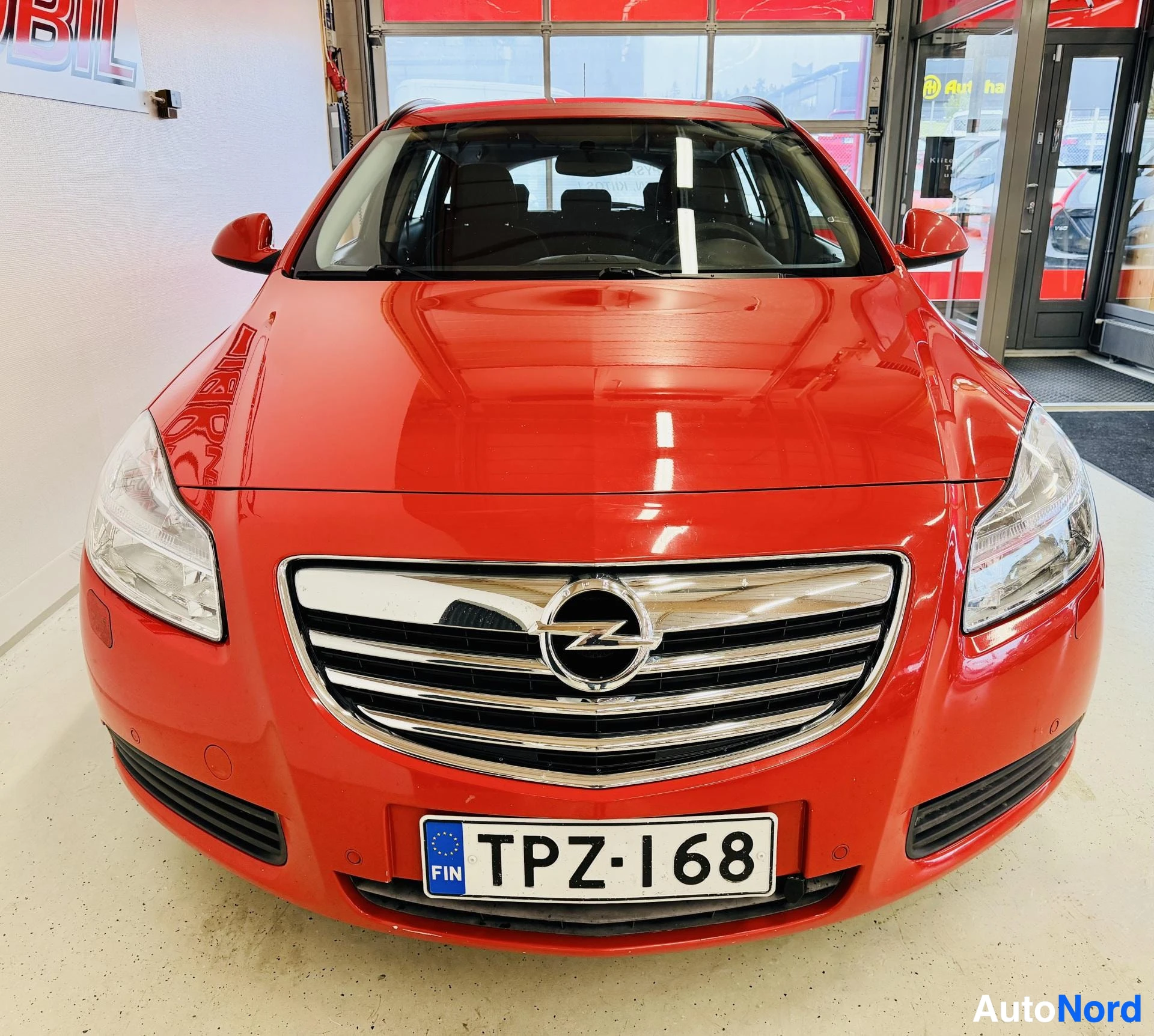 Edestä: Punainen farmariauto edestä kuvattuna. Rekisterikilvessä lukee "" ja "FIN". Etusäleikössä on Opel-logo