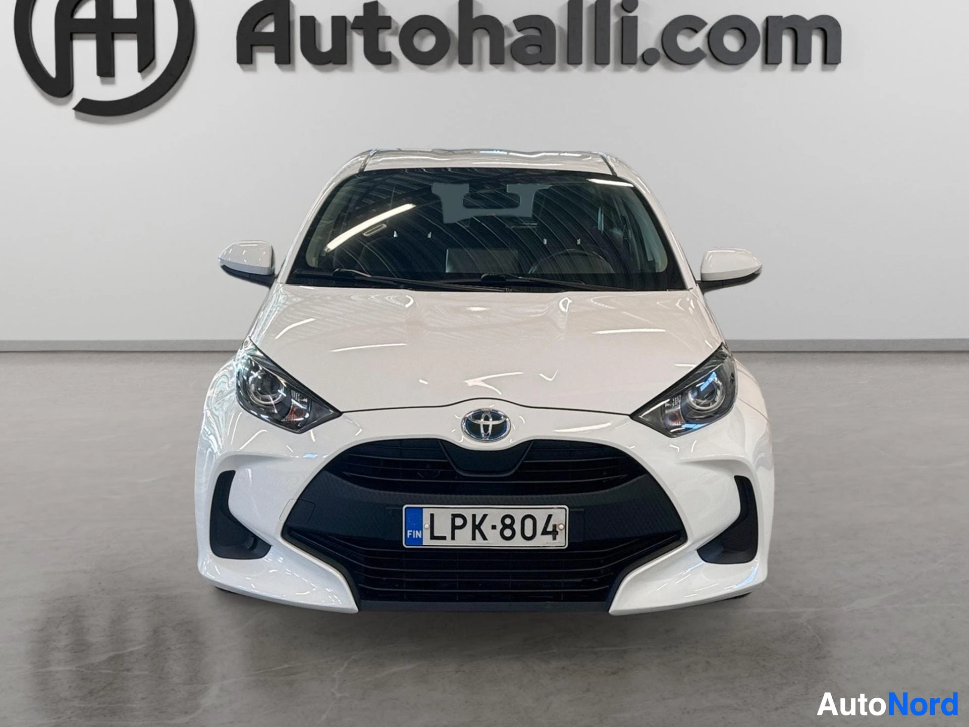 Edestä: Valkoinen Toyota Yaris edestä kuvattuna. Auton rekisterinumero on