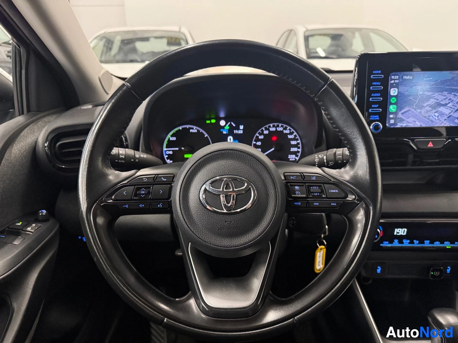 Yksityiskohta: Ohjauspyörä läheltä, Toyota-logo keskellä, näkyvät hallintapainikkeet ja mittaristo taustalla