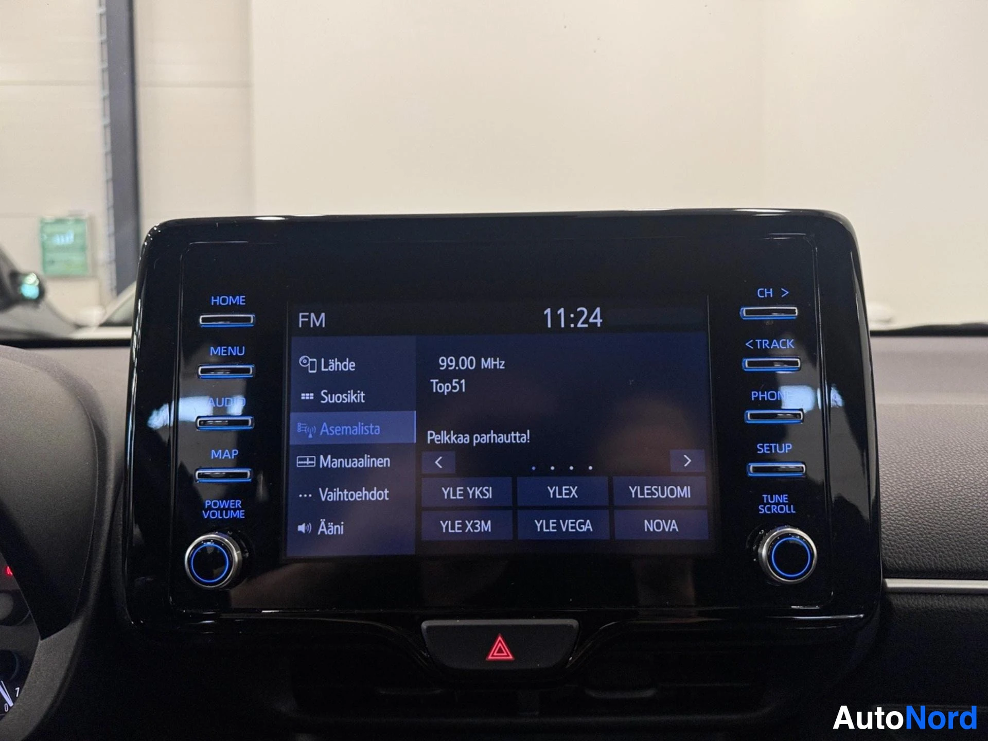 Yksityiskohta: Autovalmistajan infotainment-näyttö, jossa näkyvät FM-radio, aika 11:24 ja Bluetooth-yhteyden kaltaiset hallintavaihtoehdot.