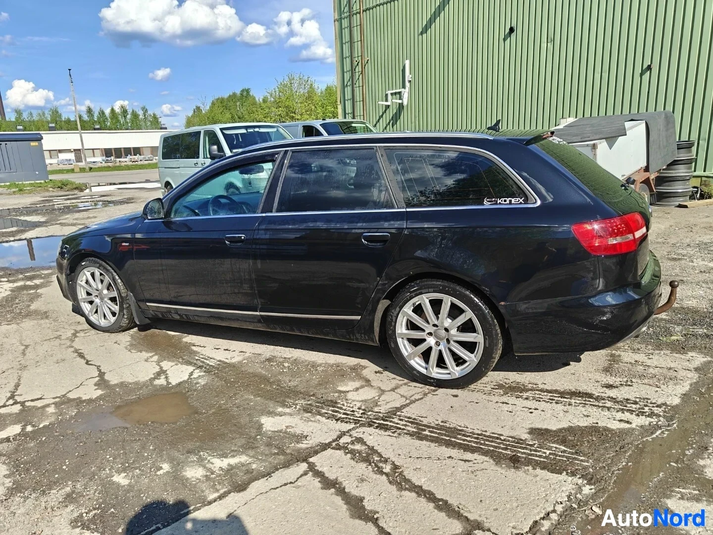 Takaviisto: Mustan farmariauton vasen kylki ja takaosa näkyvät hieman takaa. Autossa on alumiinivanteet ja vetokoukku. Takasivuikkunassa on "Vortex"-tarra.