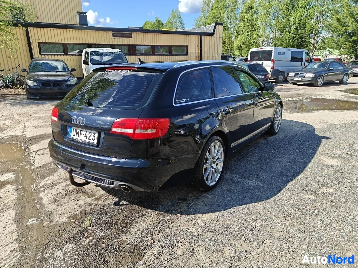 Takaviisto: Mustan farmariauton takaosa ja oikea kylki näkyvät hieman takaa. Autossa on vetokoukku ja alumiinivanteet. Rekisterikilpi on "". Takalasissa on tarroja