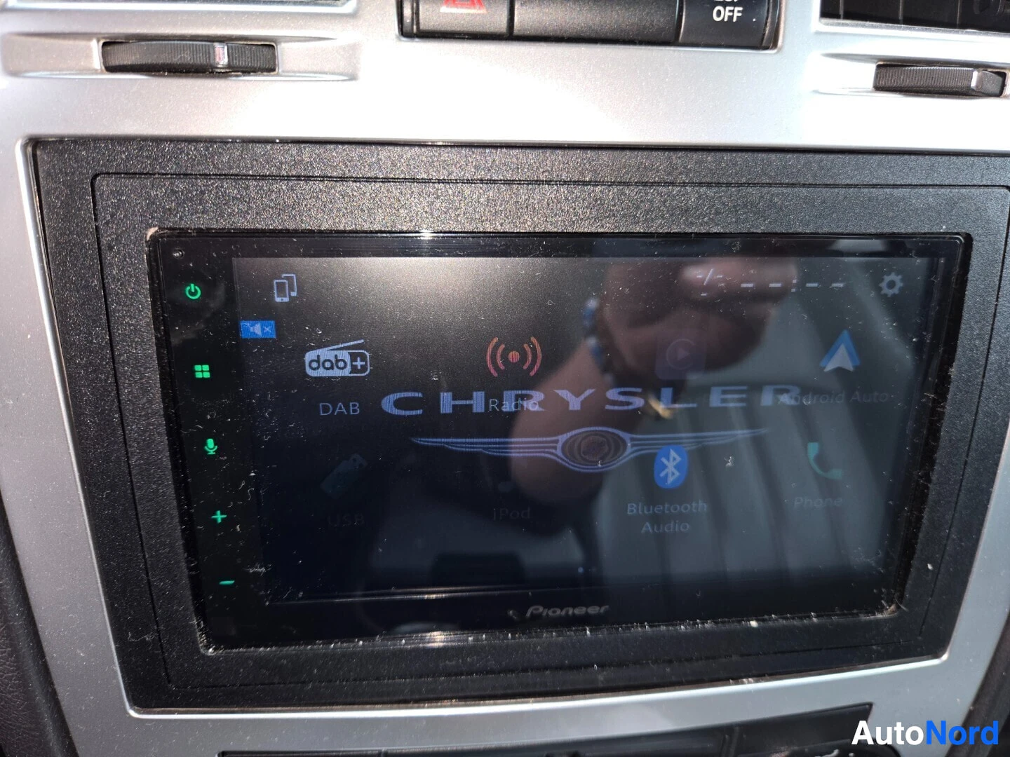 Yksityiskohta: Lähikuva auton keskinäytöstä, jossa näkyy Pioneer-logo, DAB-logo, Bluetooth Audio -kuvake ja Android Auto -teksti.