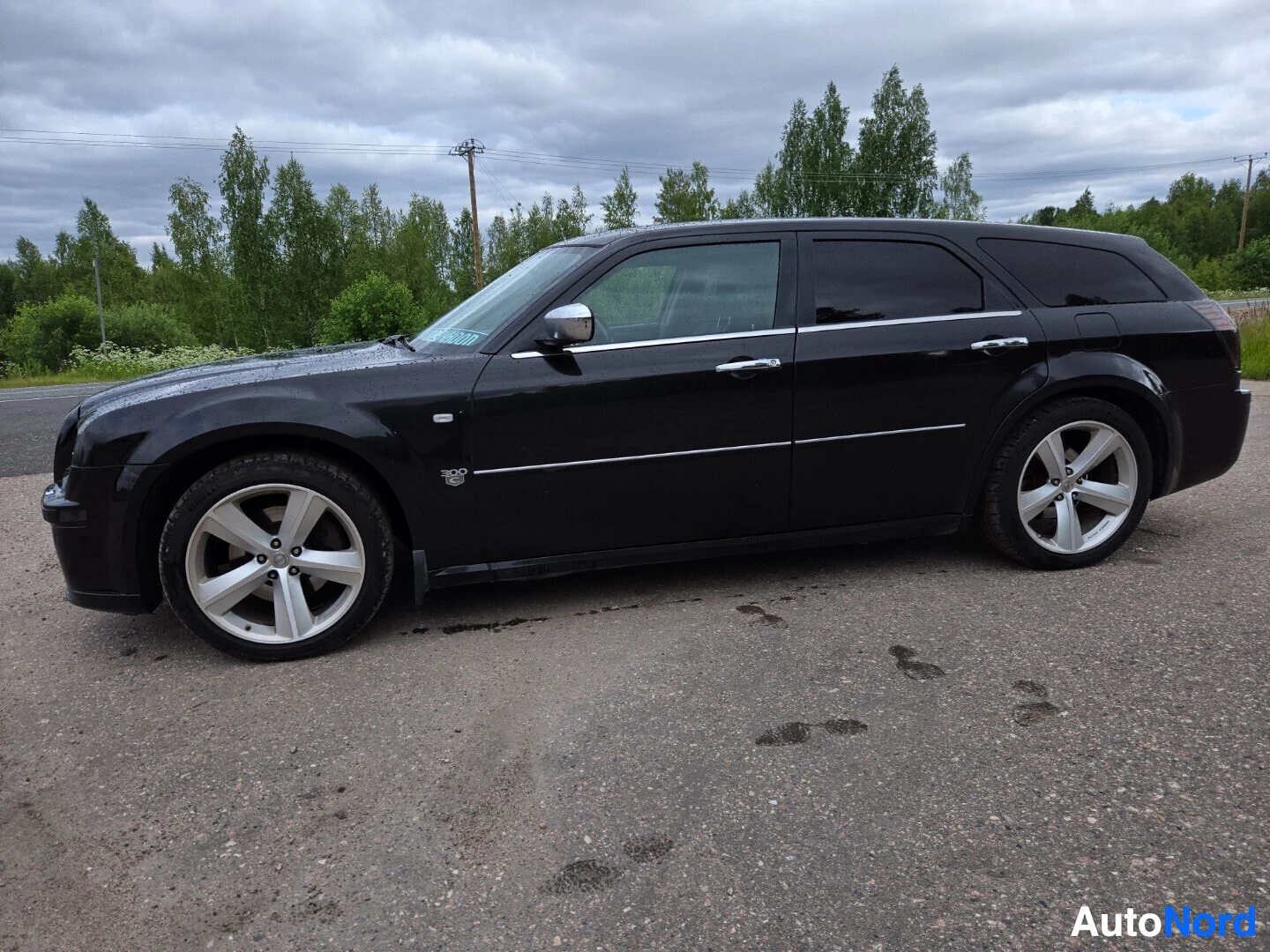 Sivulta: Musta Chrysler 300C Touring -farmariauto pysäköitynä tien sivuun, vasen kylki kuvassa, alumiinivanteet edessä ja takana.