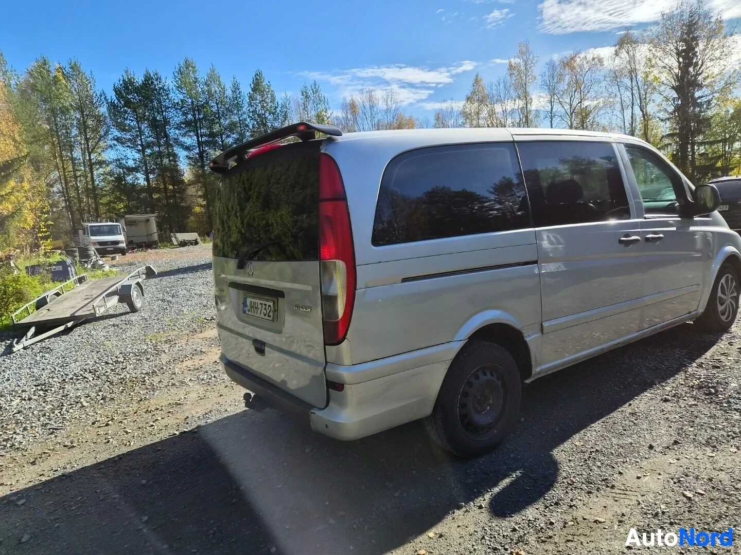 Takaviisto: Hopeanvärinen pakettiauto takaa oikealta kuvattuna. Rekisterikilpi ja tummat takalasit näkyvät. Takapyörä on musta teräsvanne