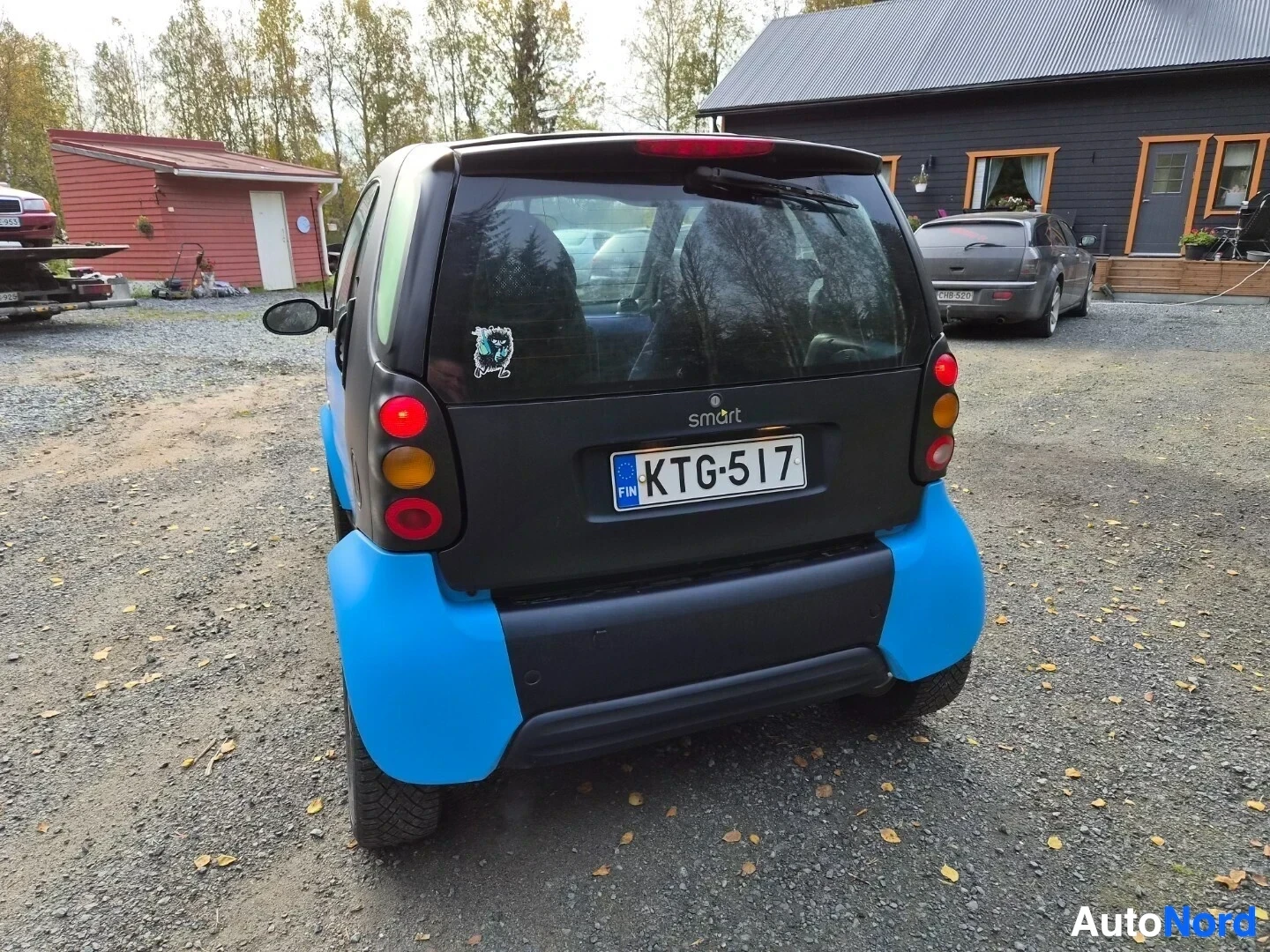 Takaa: Smart Fortwo -henkilöauton suora takakuva, jossa auto on pysäköity ulos. Autossa on siniset ja mustat paneelit, ja rekisterikilpi on näkyvissä