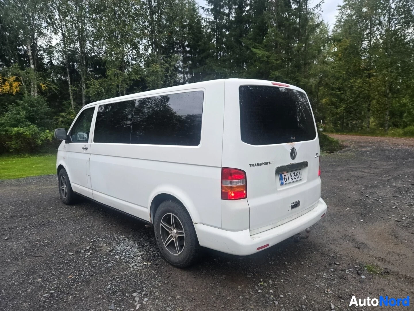 Takaviisto: Valkoinen tila-auto kuvattuna sorapihalla. Auton perässä on rekisterikilpi ja vetokoukku