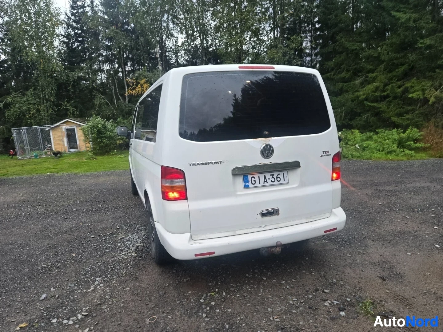 Takaa: Valkoinen tila-auto kuvattuna takaa. Takaluukussa on Volkswagen-logo, 'TRANSPORTER' teksti, 'TDI' ja '4MOTION' merkinnät. Rekisterikilpi on keskellä
