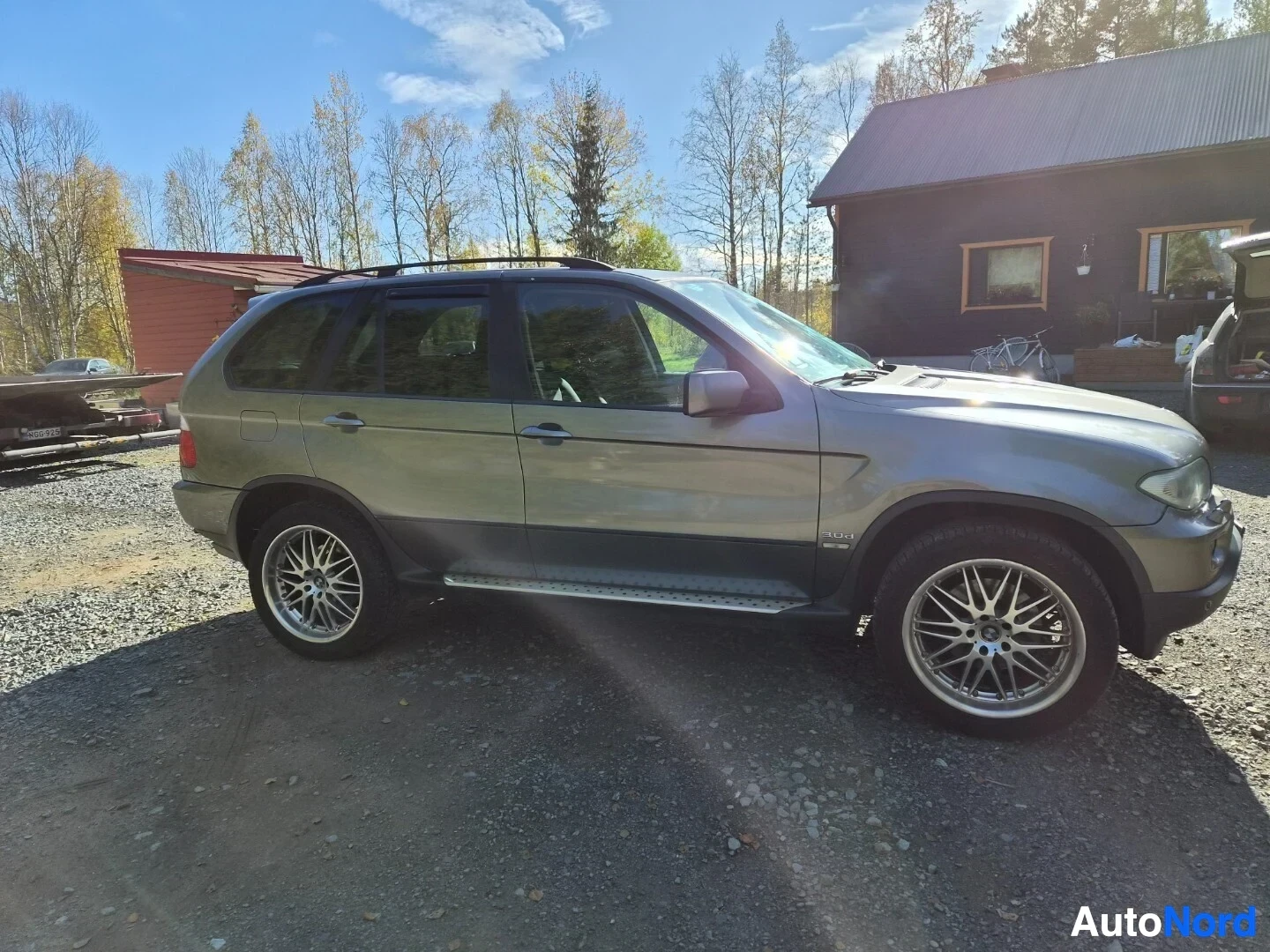Etuviisto, nokka oikealle: Harmaa SUV pysäköitynä sepelipihalla. Ajoneuvon vasen etukulma on kuvassa. Kyljessä on teksti "3.0i". Autossa on kattokaiteet, astinlaudat ja hopeanväris