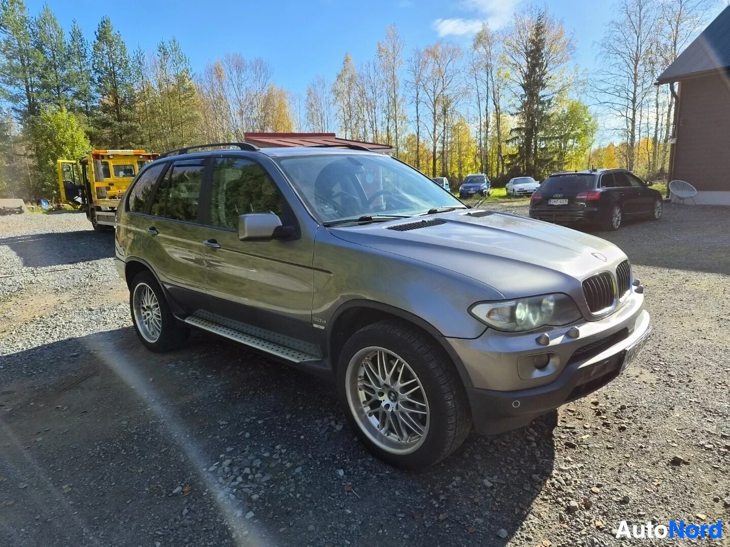 Etuviisto, nokka oikealle: Harmaa SUV pysäköitynä sepelipihalla. Ajoneuvon vasen etukulma on kuvassa. Autossa on kattokaiteet, astinlaudat ja hopeanväriset vanteet.