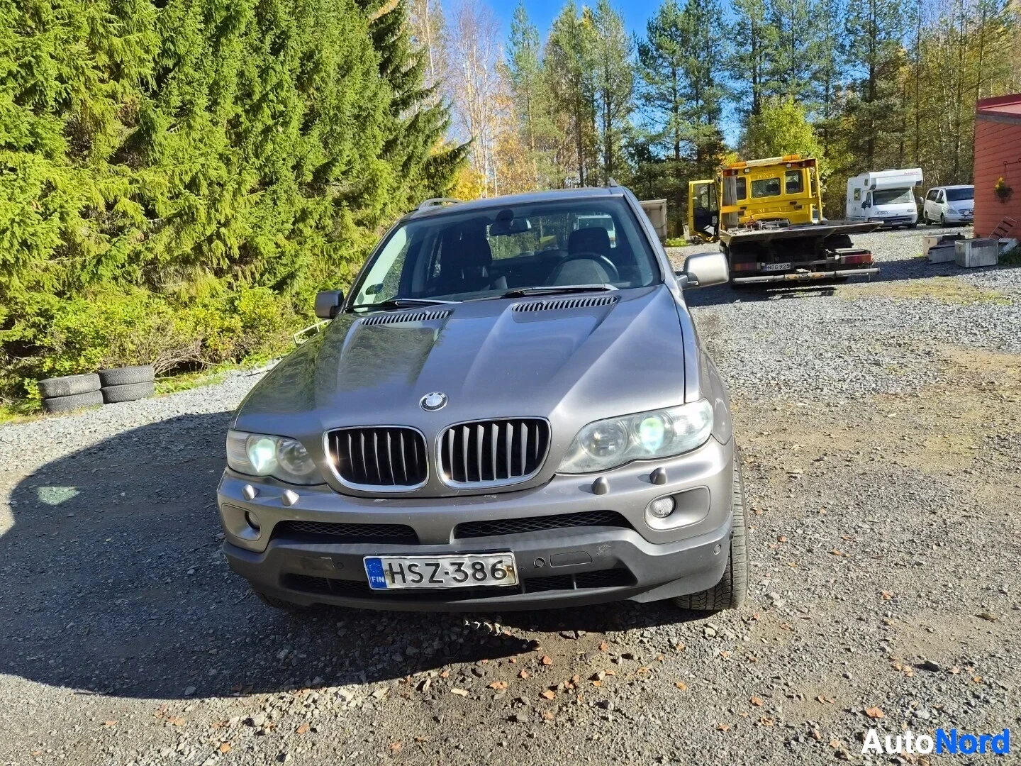 Edestä: Harmaa SUV pysäköitynä sepeliselle pihatielle, suoraan edestäpäin kuvattuna. Rekisterikilpi on näkyvissä