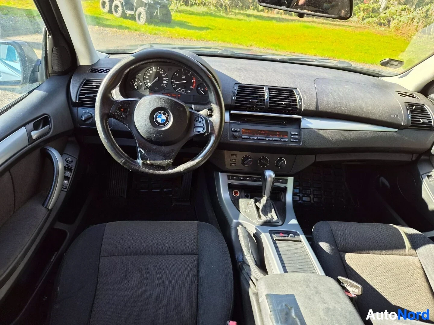 Ohjaamo: Kuvassa näkyy auton ohjaamo, jossa on musta ohjauspyörä, jossa on BMW-logo, analogiset mittarit kojelaudassa, radio-CD-soitin ja ilmastoinnin säätimet keskikons