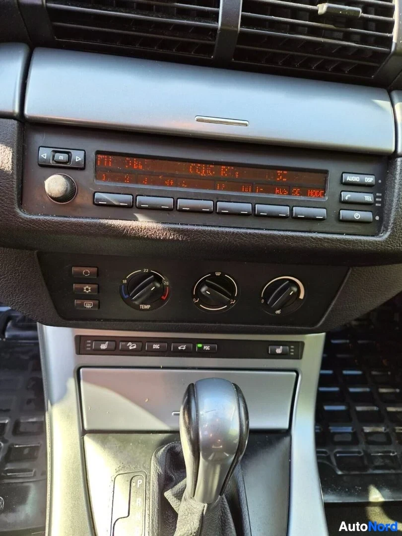 Yksityiskohta: Lähikuva auton keskikonsolista, jossa näkyy radio-CD-soitin oranssilla näytöllä, jossa lukee 'FM P3'. Sen alapuolella on kolme pyöreää nuppia, jotka ohjaavat il