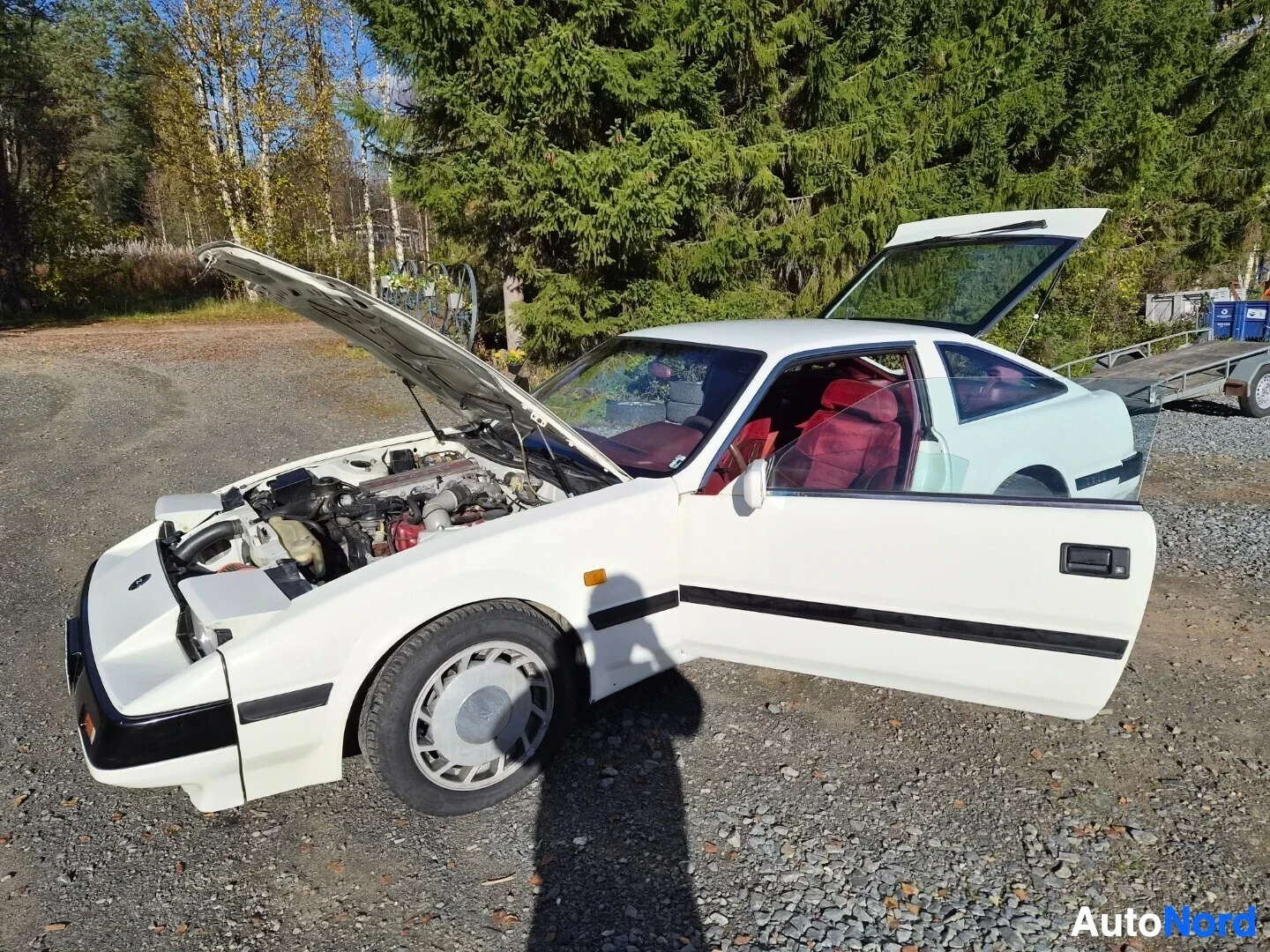 Etuviisto, nokka vasemmalle: Valkoinen Nissan 300ZX, rekisterikilpi, kuvattuna edestä ja vasemmalta sivulta. Konepelti ja molemmat ovet ovat auki. Takaluukku on myös auki