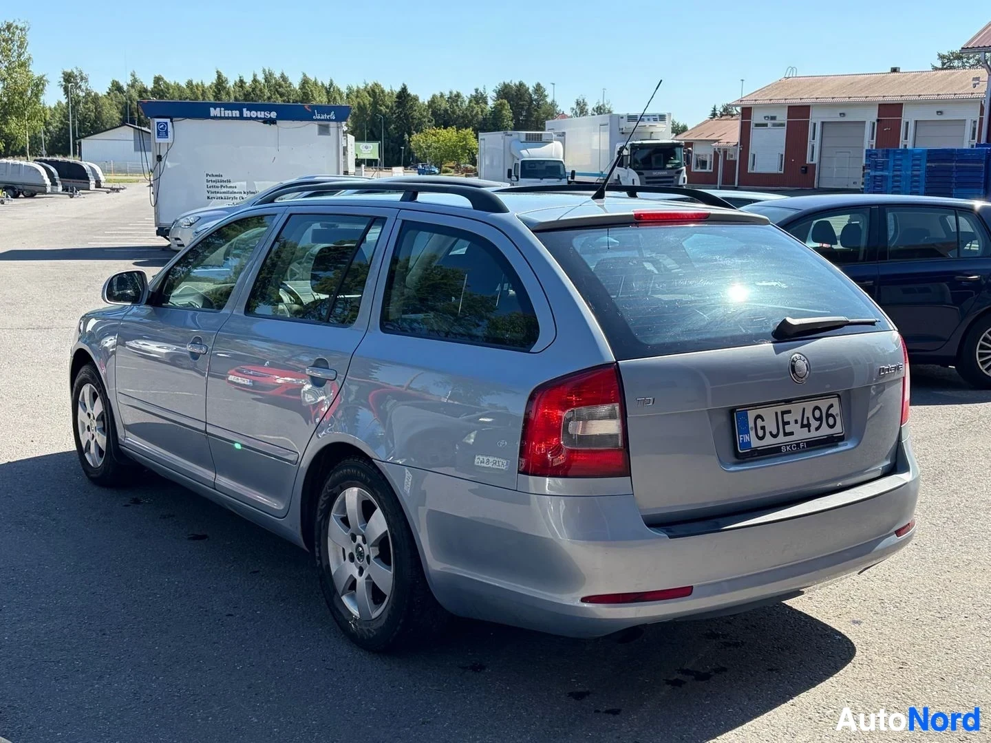 Takaviisto: Hopeanvärinen farmariauto pysäköitynä pihalle, perä ja vasen kylki kuvassa. Auton rekisterikilvessä lukee. Takaluukussa on Skoda-logo, "Octavia"-teksti