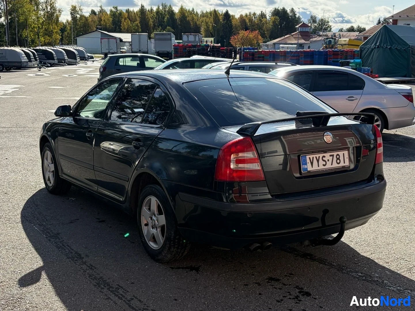 Takaviisto: Musta henkilöauto pysäköitynä takaviistosta kuvattuna. Auton rekisterinumero on. Autossa on spoileri takaluukussa ja vetokoukku