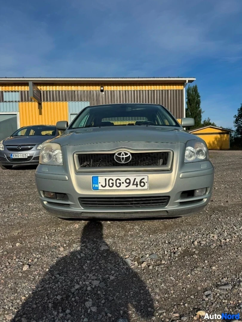 Edestä: Harmaa henkilöauto pysäköitynä sorapihalle rakennuksen eteen. Ajoneuvon etuosa on kuvattu suoraan edestä.