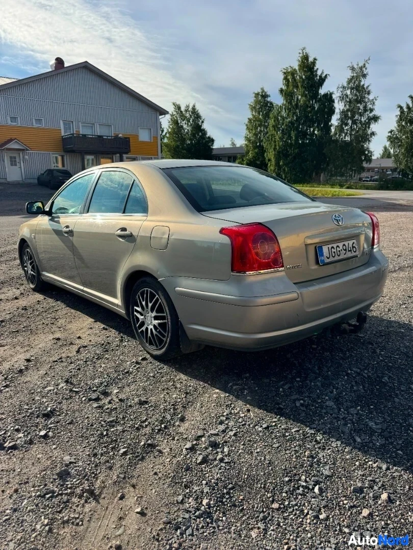 Takaviisto: Vaaleanharmaa henkilöauto takaviistosta oikealta puolelta soraparkkipaikalla. Ajoneuvon rekisterikilvessä lukee