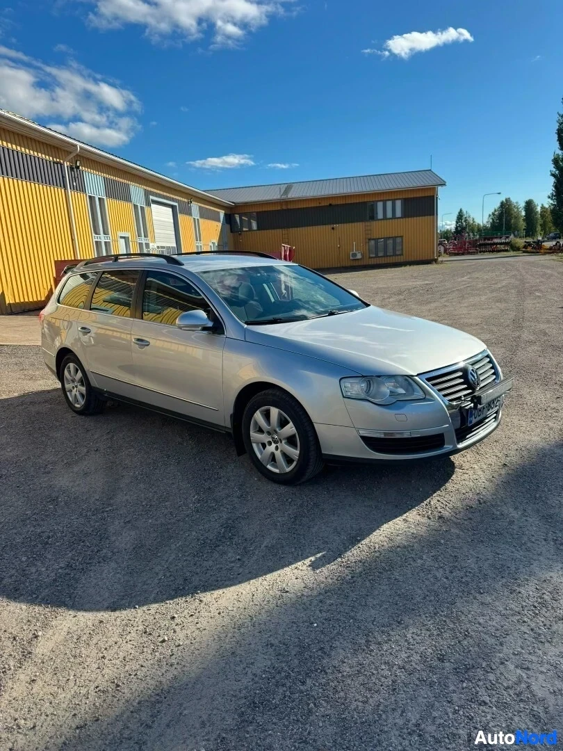Etuviisto, nokka oikealle: Hopeanvärinen farmariauto pysäköitynä sorapihalle rakennuksen eteen kirkkaassa säässä. Auton etuosa ja vasen kylki ovat näkyvissä.